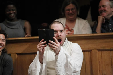 Benjamin Curns, book in hand, surprised look on his face during gulling scene, with audience laughing around him